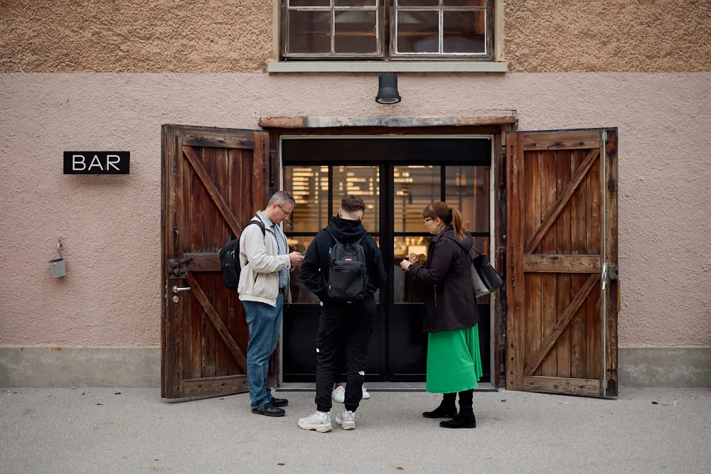 Zwei Männer und eine Frau stehen vor zwei offenen Türen vor einem Gebäude.