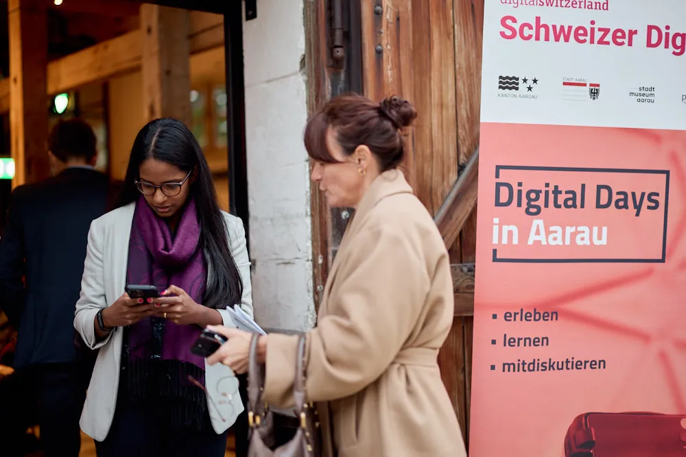 Zwei Frauen befinden sich vor einer Türe. Auf der rechten Seite befindet sich ein Roll-Up des Events.