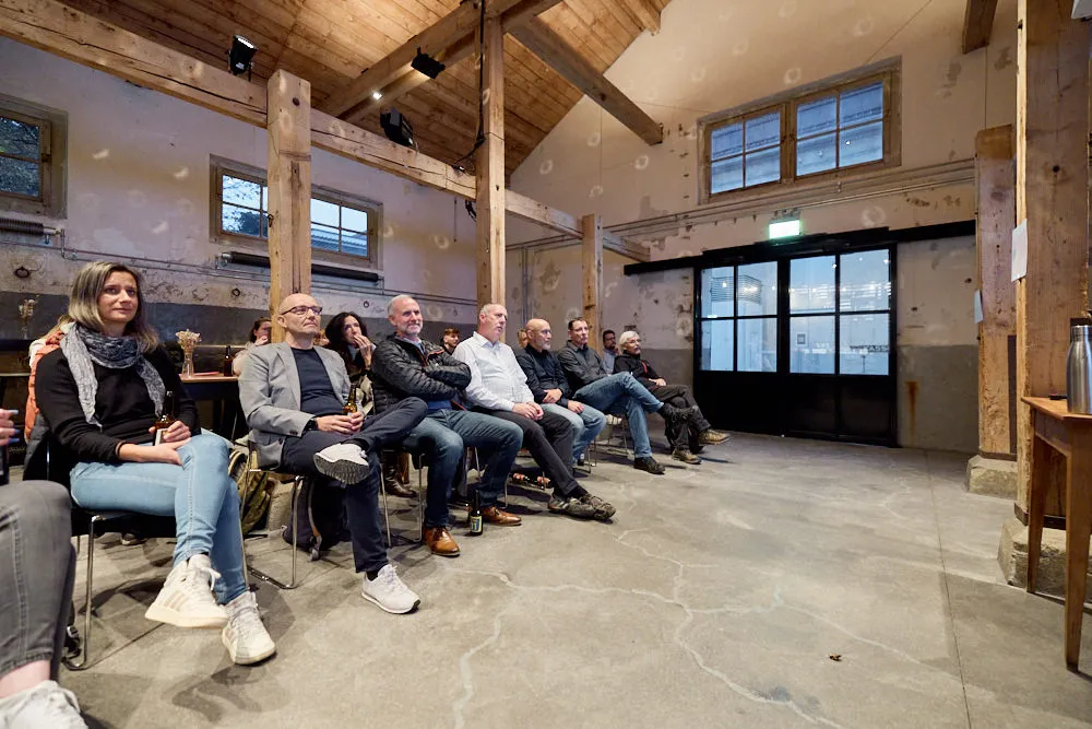 Ein Publikum sitzt in einem Gebäude auf Stühlen.