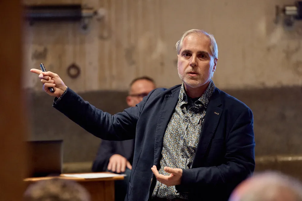 Ein Mann hält eine Präsentation und zeigt mit einem Stift in der Hand auf die Seite.