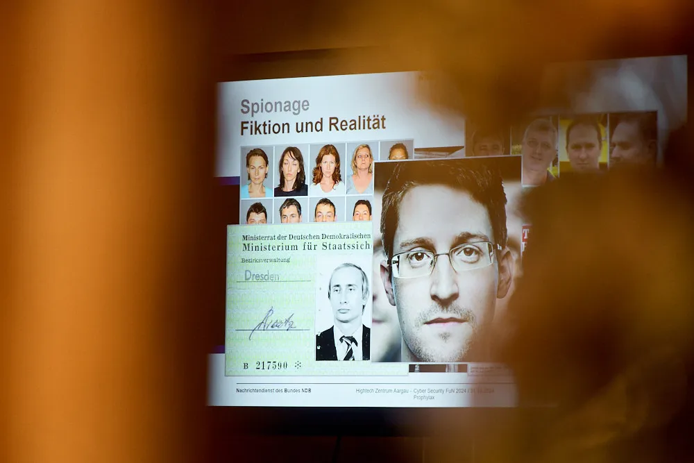 Ein Bildschirm auf dem eine Präsentation gezeigt wird. Auf dem Bildschirm sind Portraitbilder und Text ersichtlich. Der Titel lautet Spionage Fiktion und Realität.