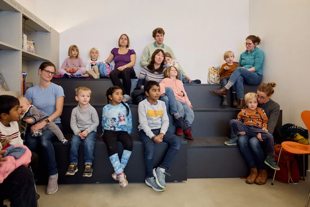 Eltern und Kinder auf einer Tribüne hören gespannt zu.
