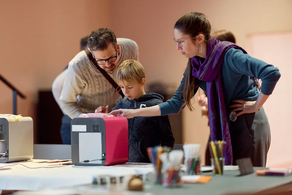 Ein Mann und eine Frau bedienen mit einem Jungen einen würfelförmigen Apparat.