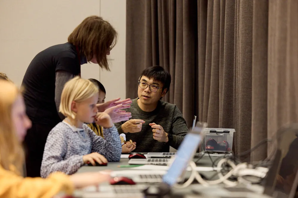 Eine Frau erklärt einem Mann und einem Kind etwas an einem Laptop.