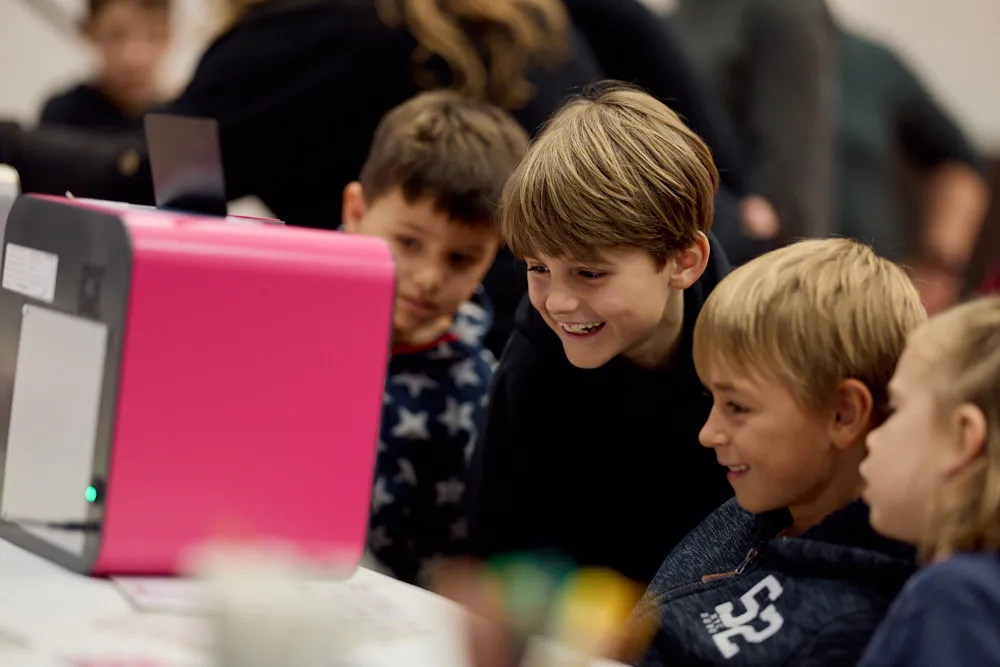 Kinder schauen gespannt in einen 3D-Drucker.