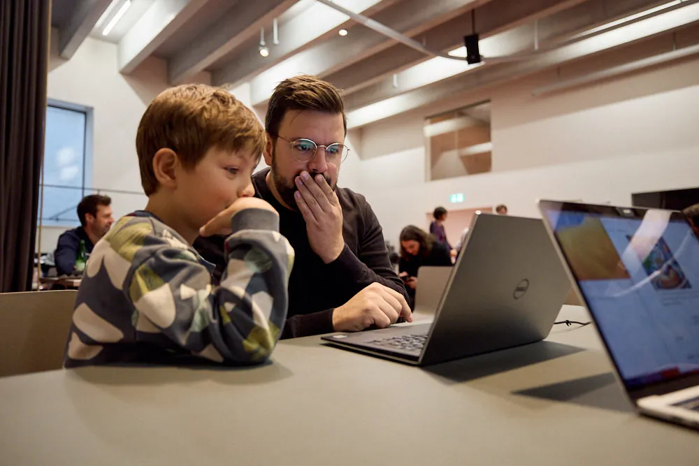 Ein Mann mit einem Jungen schauen konzentriert in den Laptop.