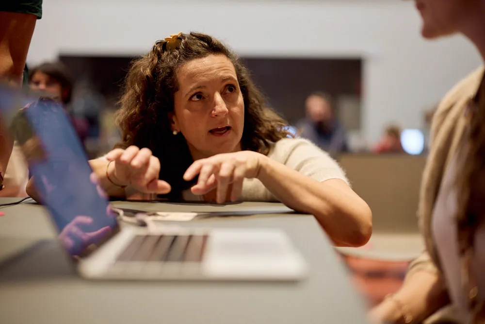 Eine Frau erklärt Menschen an einem Laptop etwas.