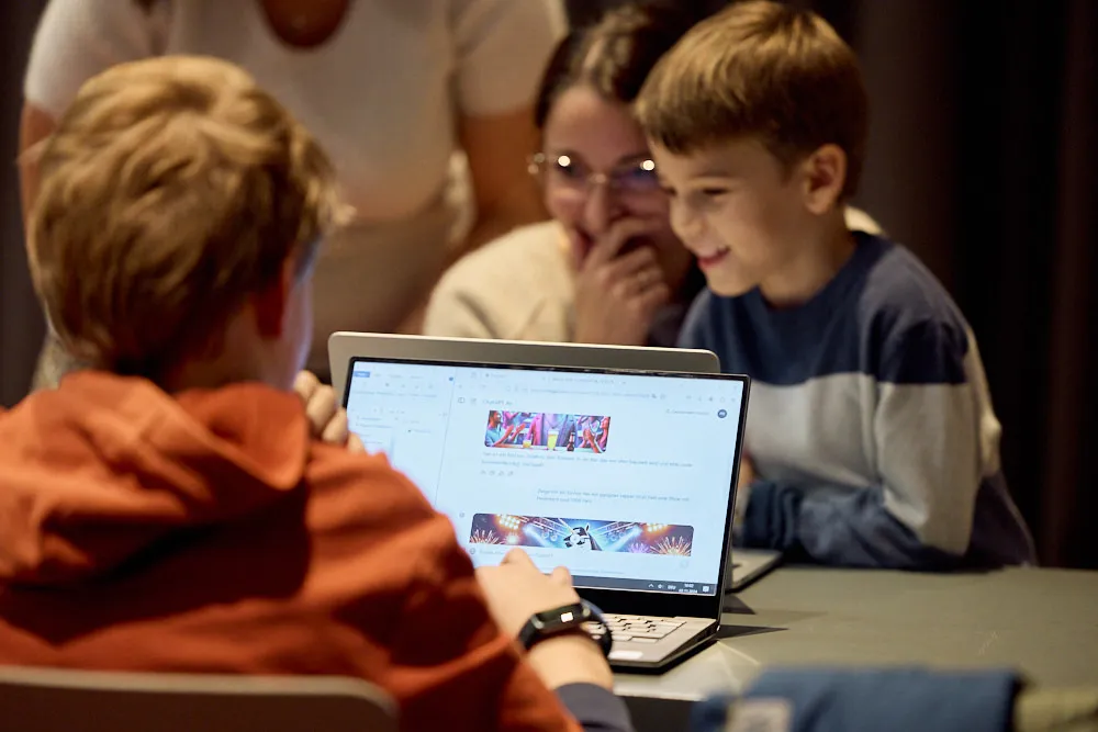 Kinder mit erwachsenen Personen bedienen lächelnd Laptops.