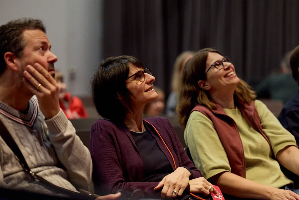 Ein Mann und zwei Frauen schauen gespannt und lächelnd nach schräg oben.