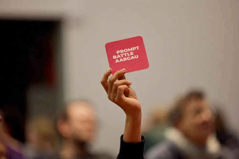 Eine Hand hält ein Getränkeuntersetzer mit dem Text Prompt Battle Aargau in die Höhe.