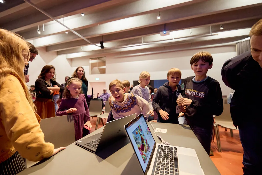 Kinder und Erwachsene schauen gespannt in zwei Laptops.