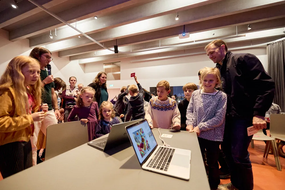 Kinder und Erwachsene schauen gespannt in zwei Laptops.