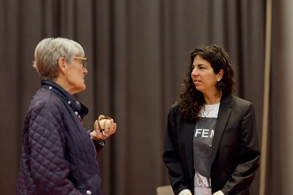 Zwei Frauen sprechen vor einem Vorhang miteinander.