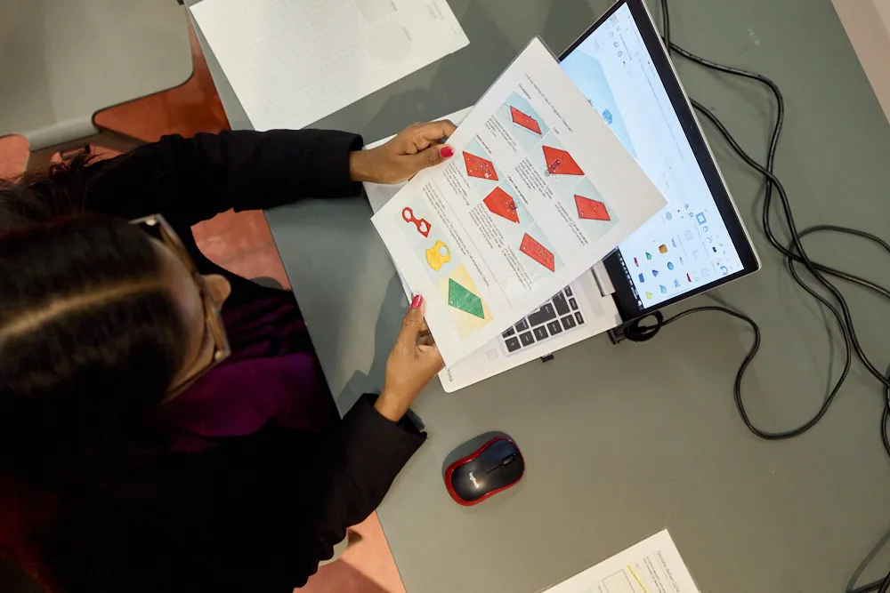 Eine Frau liest vor einem Laptop eine Anleitung auf Papier.