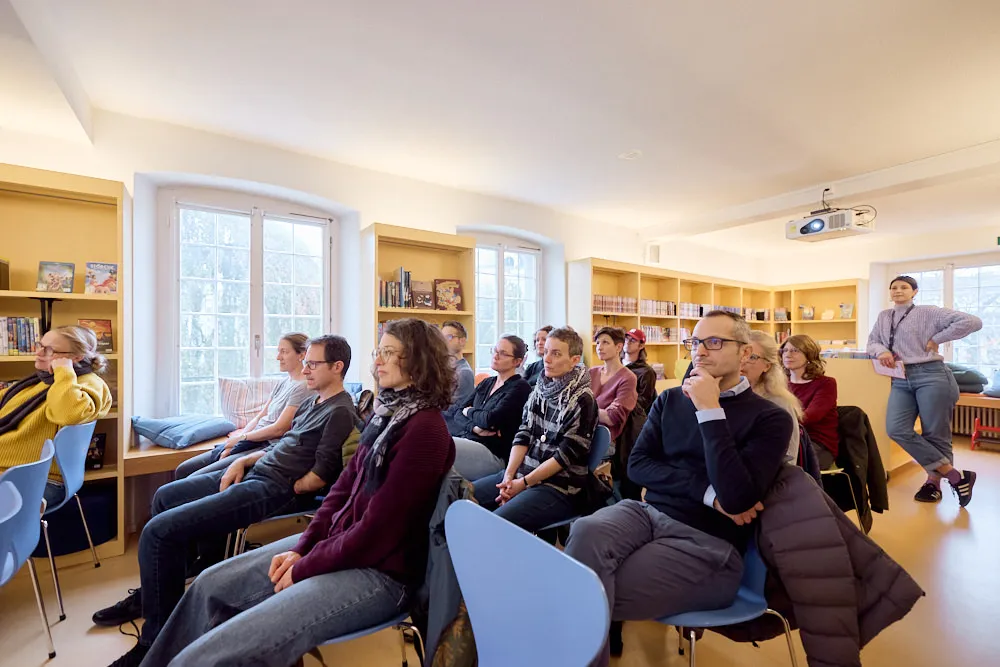 Ein Publikum sitzt in einer Bibliothek und hört gespannt zu.