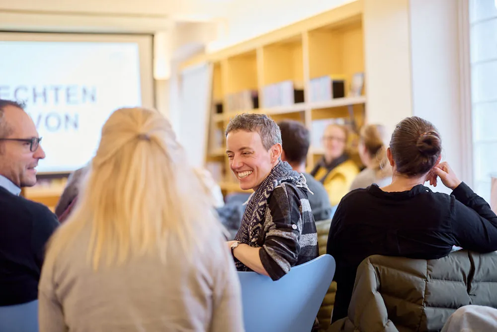Zwei Frauen und ein Mann sprechen im Publikum miteinander und sie lächeln sich an.