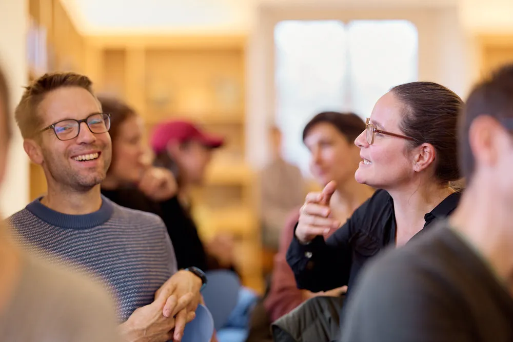Menschen im Publikum sprechen miteinander. Sie lächeln und sehen interessiert aus.