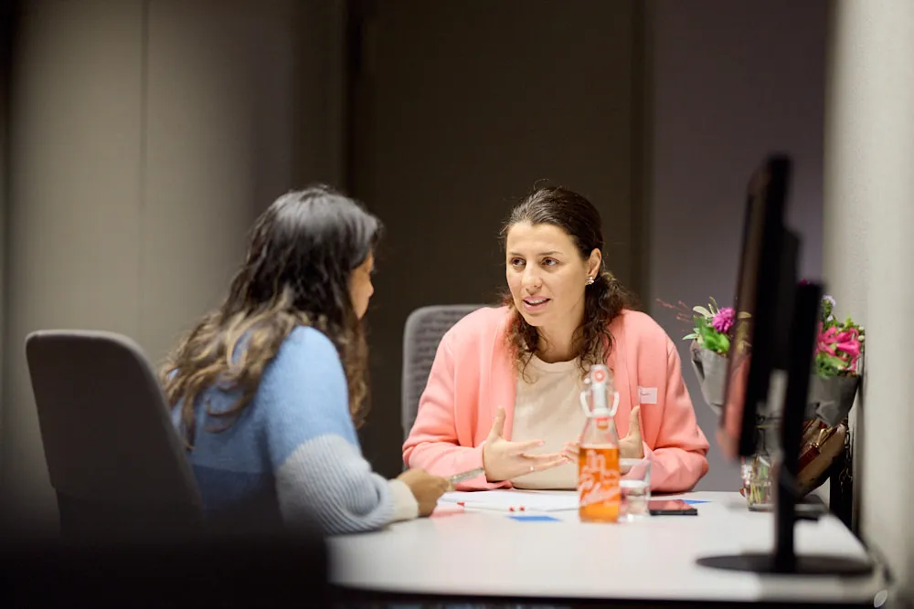 Zwei Frauen an einem Tisch sprechen miteinander.
