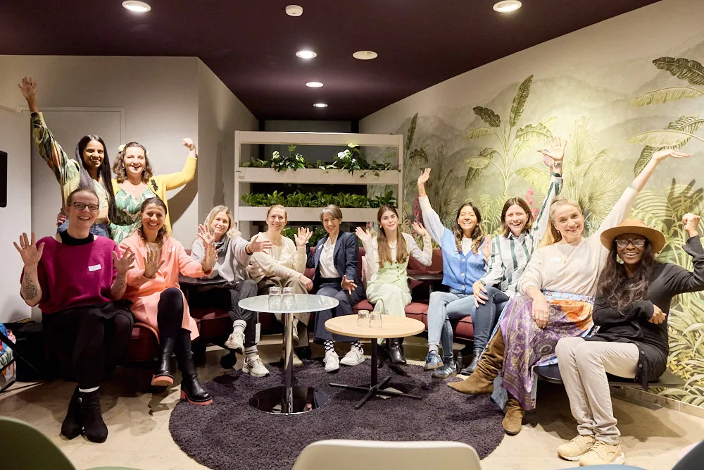 Eine Gruppe Frauen schauen lächelnd in die Kamera. Zwei Frauen stehen hinter zehn sitzenden Frauen. Sie jubeln und halten die Hände in die Höhe.