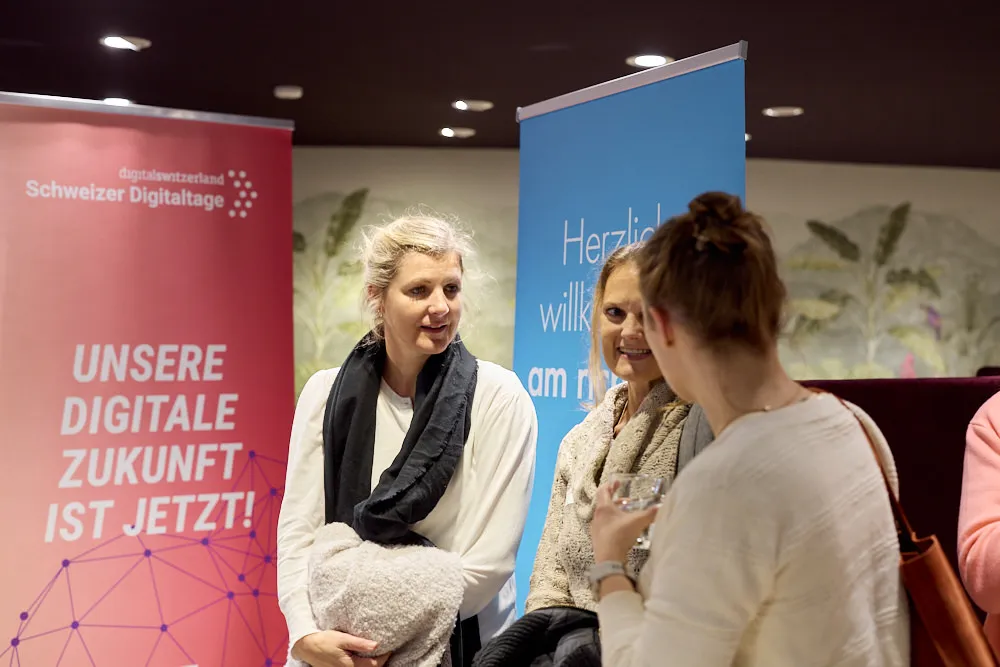 Drei Frauen sprechen vor zwei Roll-Ups des Events miteinander.