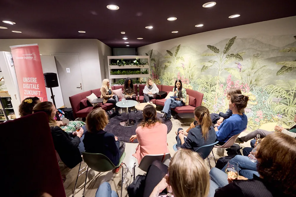 Vier Frauen sitzen auf einem Sofa und halten eine Präsentation vor einem sitzenden Publikum.