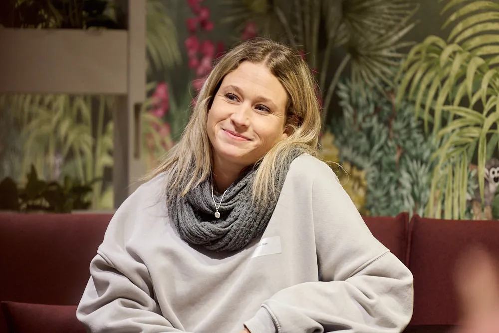 Eine Frau auf dem Sofa hört gespannt und lächelnd zu.