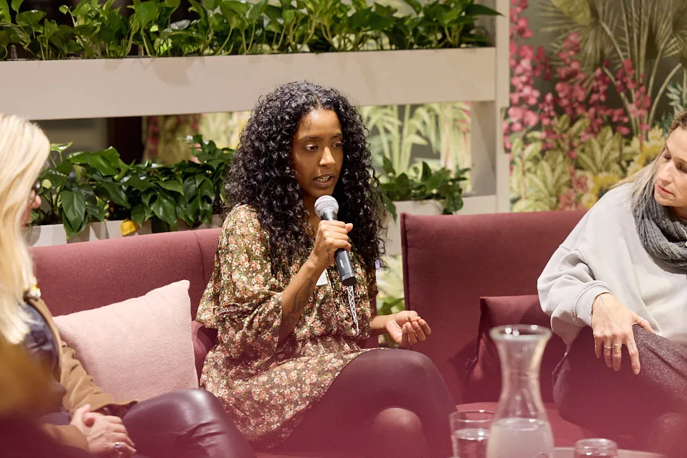 Eine Frau auf dem Sofa hält ein Mikrofon und spricht zum Publikum.