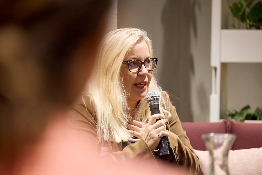 Eine Frau auf dem Sofa hält ein Mikrofon und spricht zum Publikum.