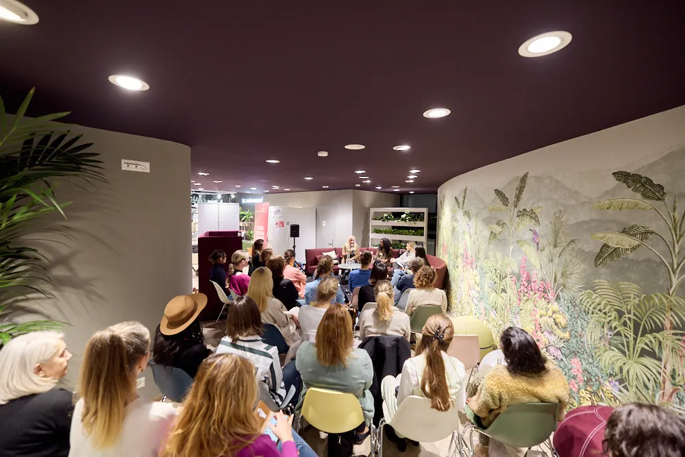 Vier Frauen sitzen auf einem Sofa und halten eine Präsentation vor einem sitzenden Publikum.