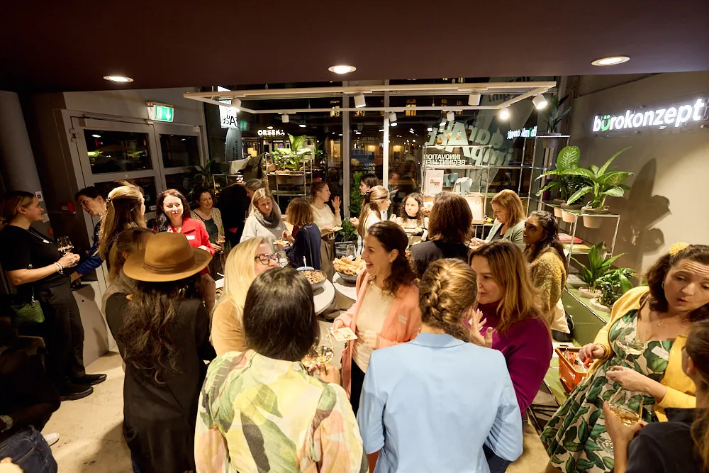 Frauen unterhalten sich im Stehen. Auf Tischen befinden sich Snacks und Getränke.