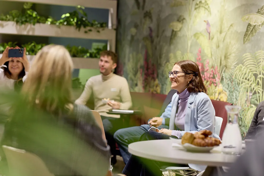 Menschen sitzen an Tischchen mit Brötchen und hören gespannt zu.