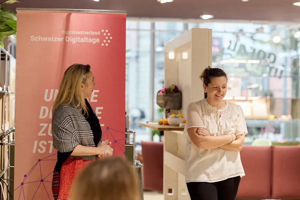 Zwei Frauen sprechen lächelnd vor einem Publikum miteinander.