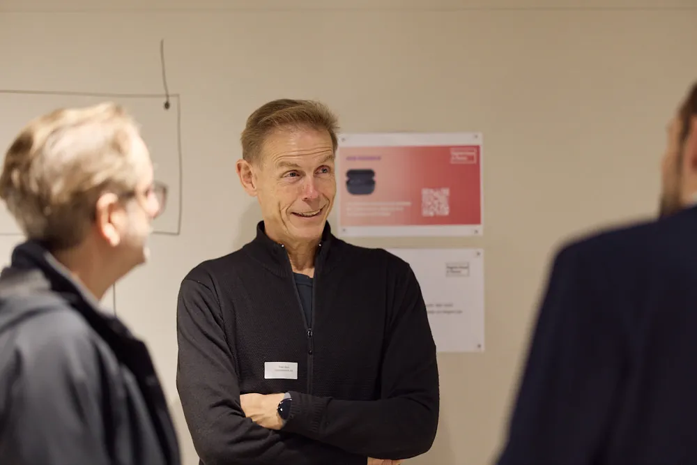 Drei Männer sprechen miteinander. Der Mann in der Mitte schaut ein wenig erstaunt, aber lächelt.