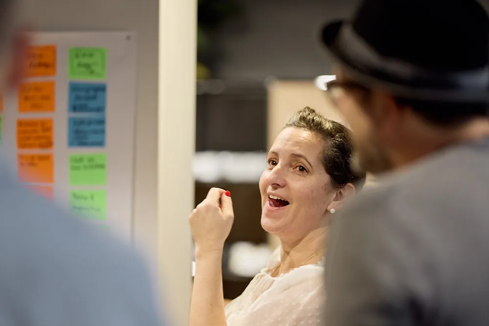Eine Frau lächelt und erzählt dem Publikum etwas. Sie steht vor einer Wand mit Post-Its.