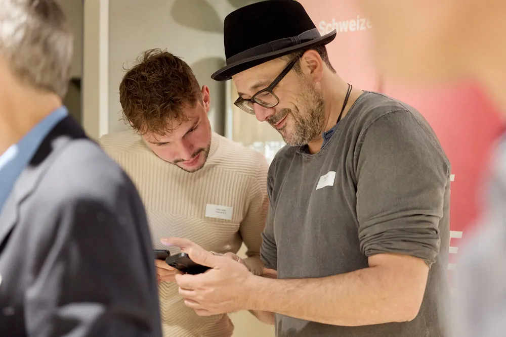 Zwei Männer an jeweils einem Smartphone schauen auf das Smartphone des Mannes im Vordergrund.