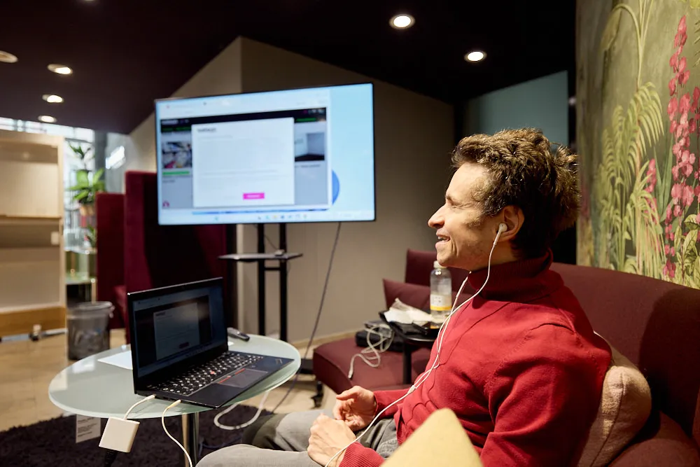 Ein Mann sitzt mit Kopfhörern vor einem Laptop und lächelt.