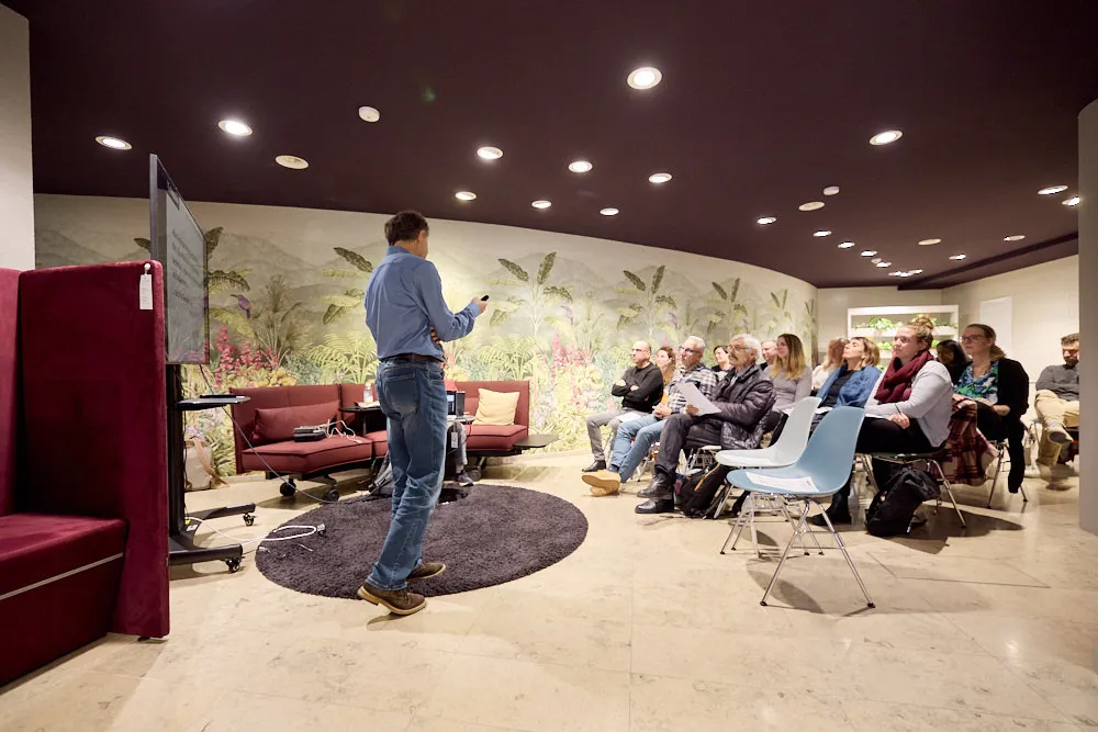 Ein Mann hält eine Präsentation vor einem Bildschirm vor einem sitzenden Publikum.