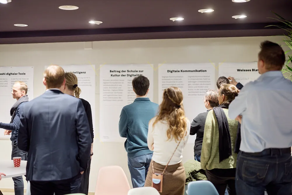 Menschen stehen vor einer Wand mit Plakaten mit verschiedenen Inhalten.