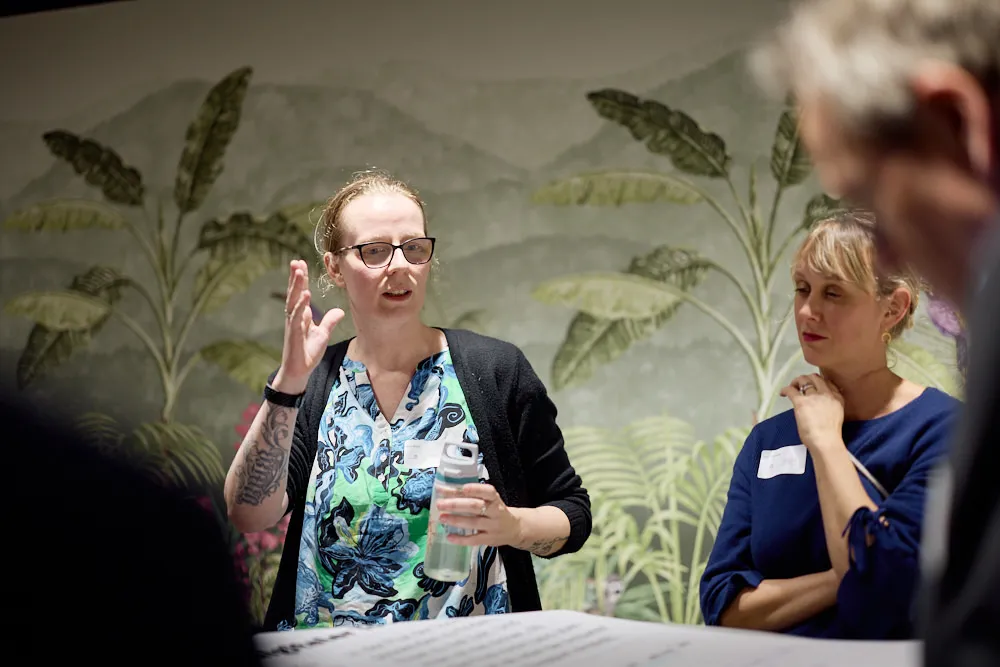 Eine Frau spricht stehend zu einem stehenden Publikum.