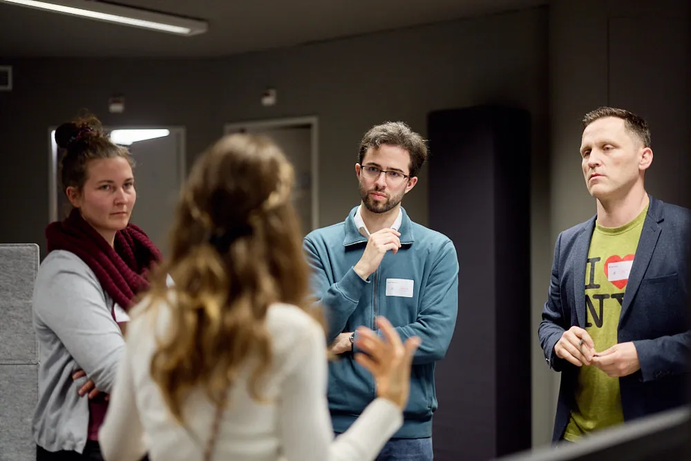 Eine Frau spricht zu stehenden Menschen. Sie hören gespannt zu.
