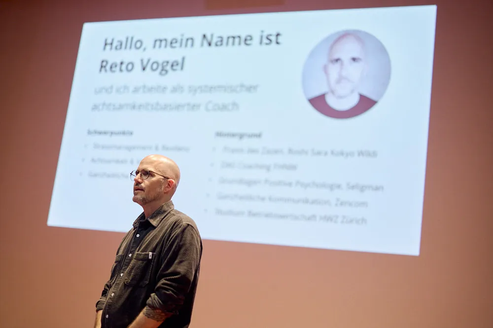 Ein Mann hält eine Präsentation vor einer Leinwand. Auf der Leinwand wird seine Präsentation projiziert.