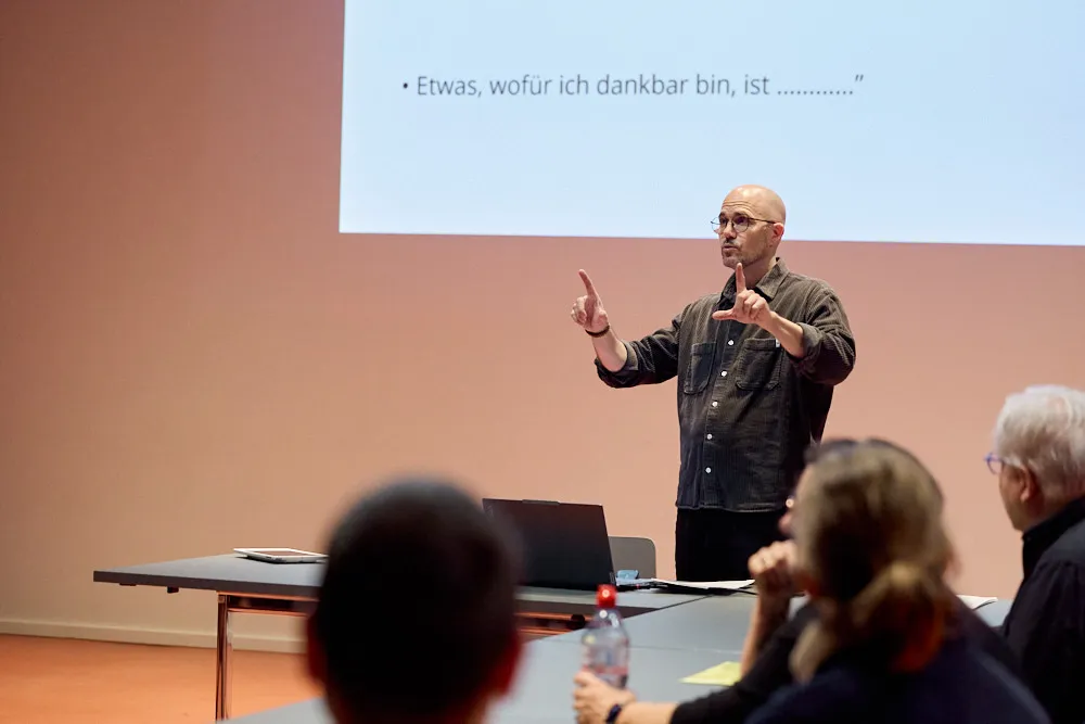 Ein Mann hält eine Präsentation vor einer Leinwand vor einem Publikum. Auf der Leinwand wird seine Präsentation projiziert.