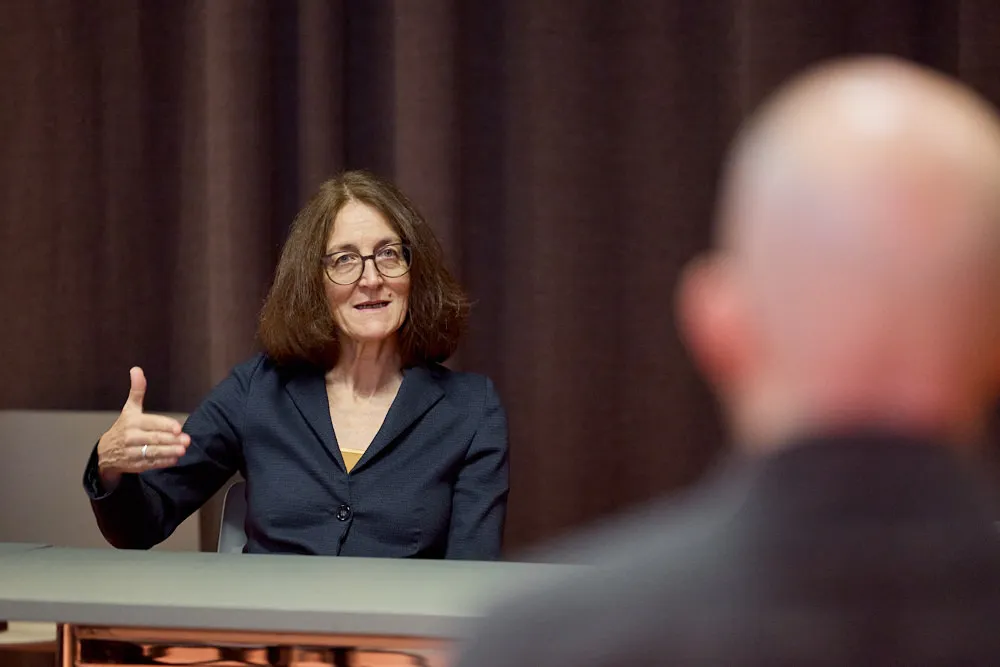 Eine Frau sitzt an einem Tisch und spricht zu einem Mann vor ihr.
