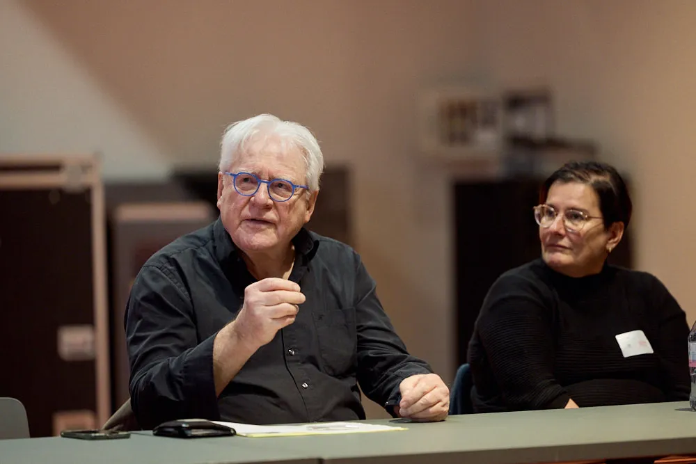 Ein Mann und eine Frau sitzen an einem Tisch. Der Mann sprich und gestikuliert mit einer Hand. Die Frau hört ihm zu.