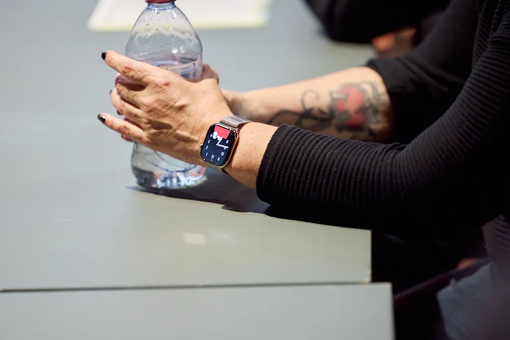 Eine Frau hält eine Wasserflasche mit beiden Händen. An ihrem Handgelenk ist eine Smartwatch.