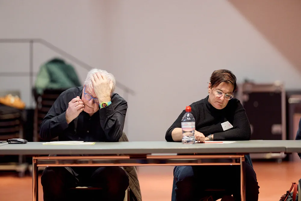 Ein Mann und eine Frau sitzen an einem Tisch und füllen ein Papier aus. Sie sehen konzentriert aus.