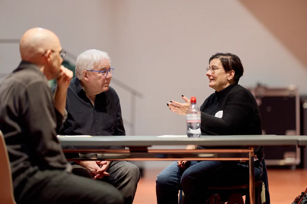 Eine Frau spricht zu zwei Männern. Die Männer hören ihr gespannt zu.