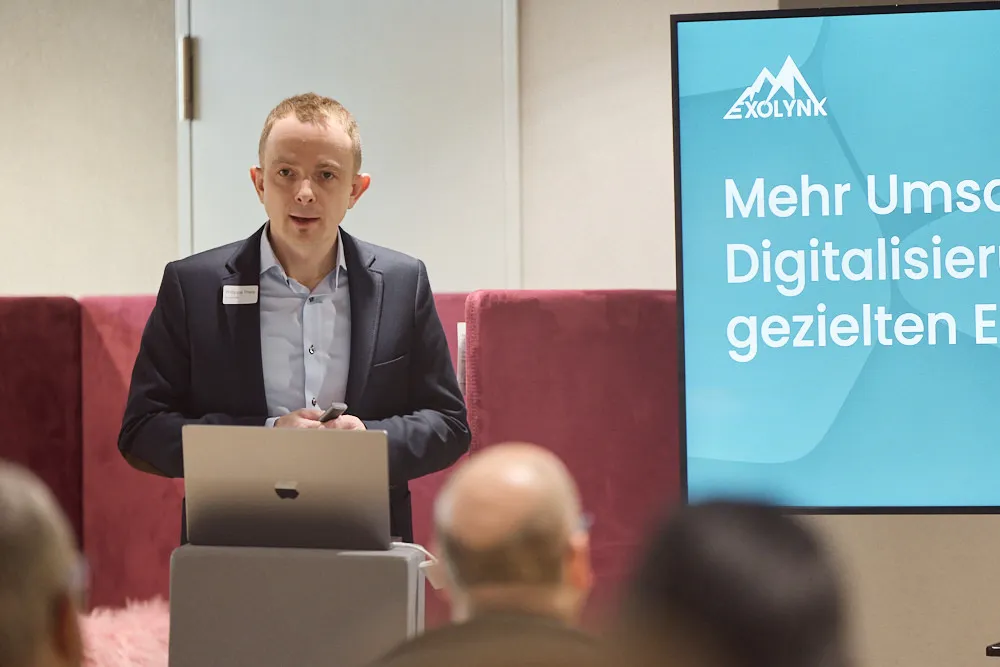 Ein Mann hält vor einem Publikum eine Präsentation. Auf dem Bildschirm hinter ihm befindet sich seine Präsentation.