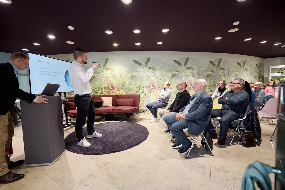 Zwei Männer halten vor einem Publikum eine Präsentation.