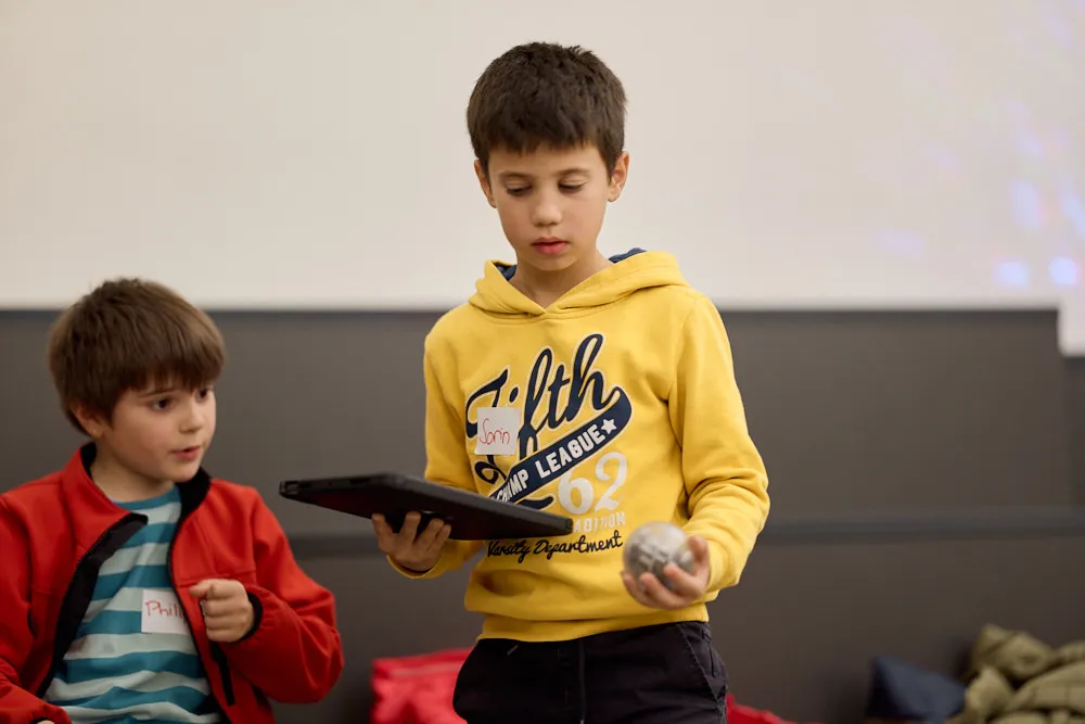 Zwei Kinder bedienen mit einem Tablet einen kleinen Roboter.
